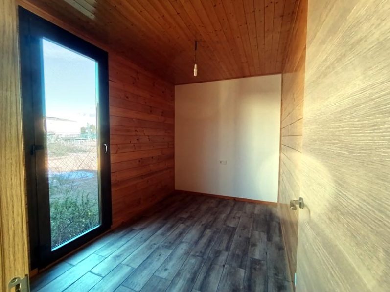 Interior de un espacio con paredes de madera, una ventana y suelo de madera oscura.