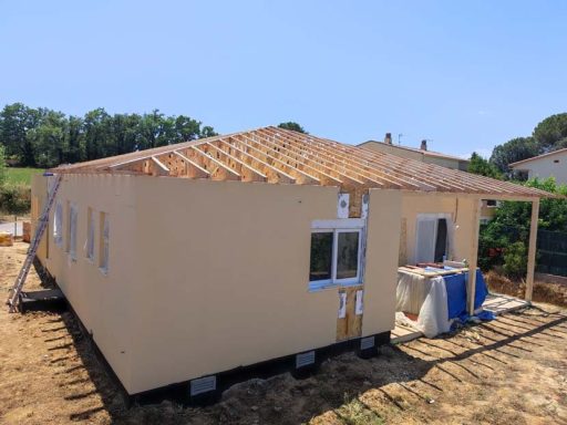 Casa en construcción con techo a dos aguas y paredes de color beige.