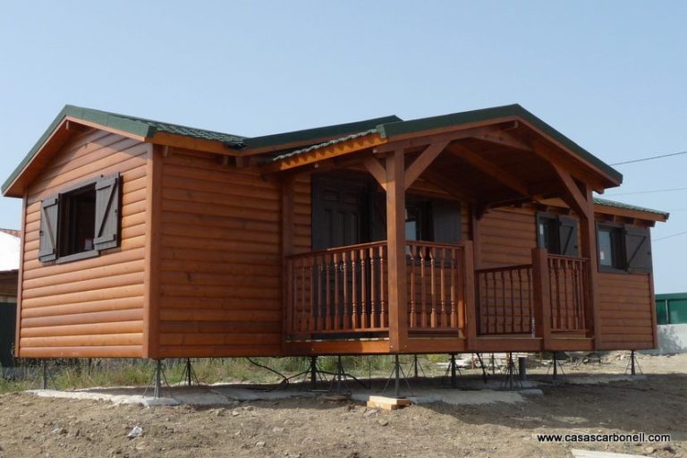 Casa prefabricada de madera con porche, ventanas oscuras y tejado a dos aguas.