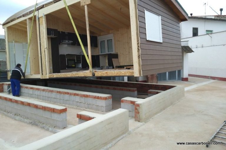 Casa prefabricada siendo levantada con grúas sobre una base de cemento.