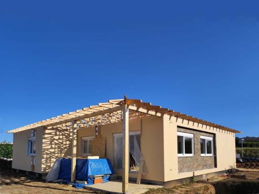 Casa en construcción con techado simple, paredes de piedra y cielo despejado.
