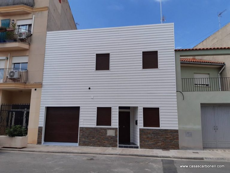 Casa prefabricada adosada de dos plantas con fachada blanca y detalles en piedra, ventanas oscuras.