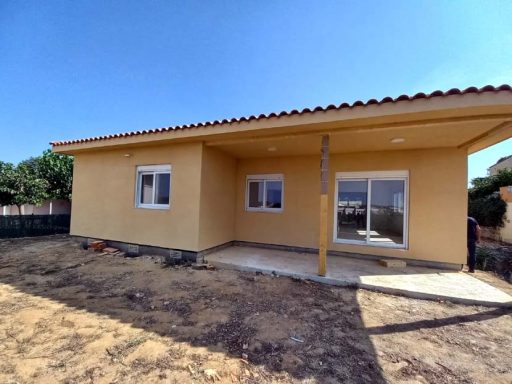 Vista exterior de una casa amarilla con patio, ventanas y cielo azul despejado.