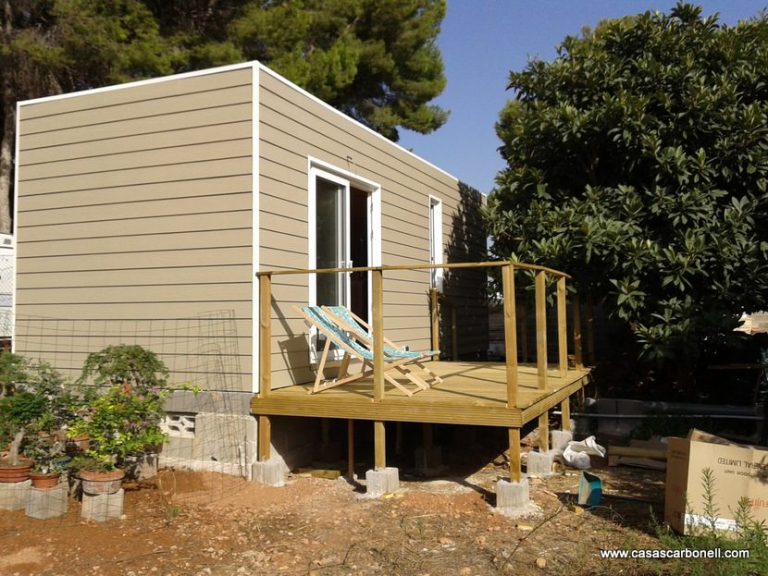 Casa contenedor prefabricada con balcón, rodeada de vegetación y árboles.