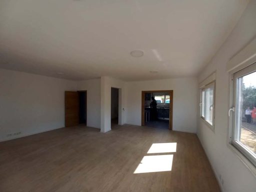 Interior de una habitación vacía con paredes blancas y ventanas, suelo de madera clara.