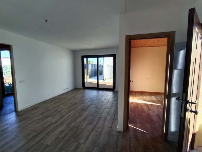 Sala amplia y luminosa con suelo de madera y puertas abiertas a un patio exterior.