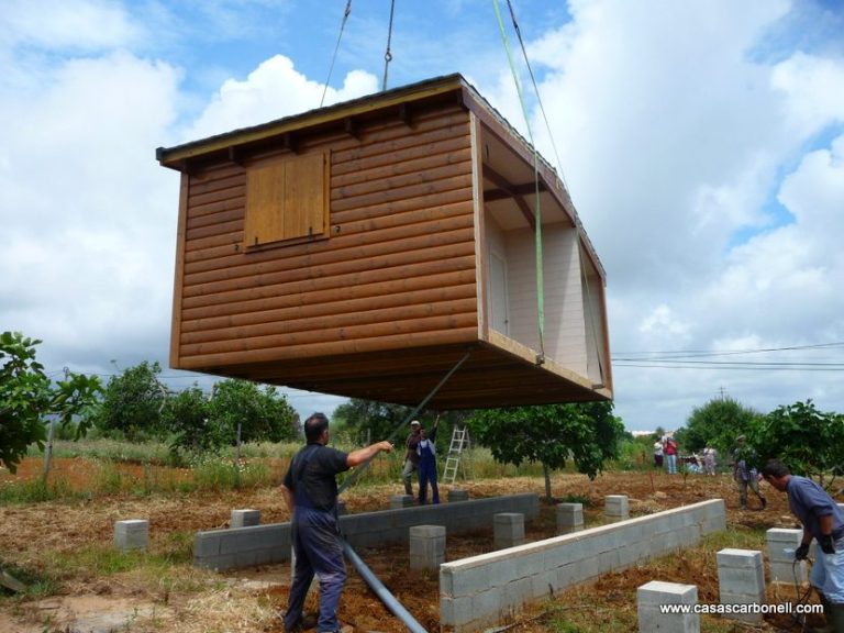El proceso de construcción con casas prefabricadas modulares siendo levantada por grúas sobre cimientos en un entorno rural.