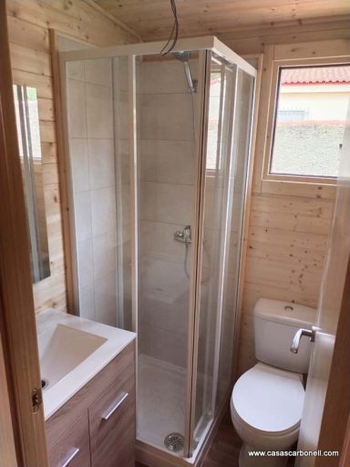 Baño pequeño con ducha de cristal, lavabo y WC en un ambiente de madera.