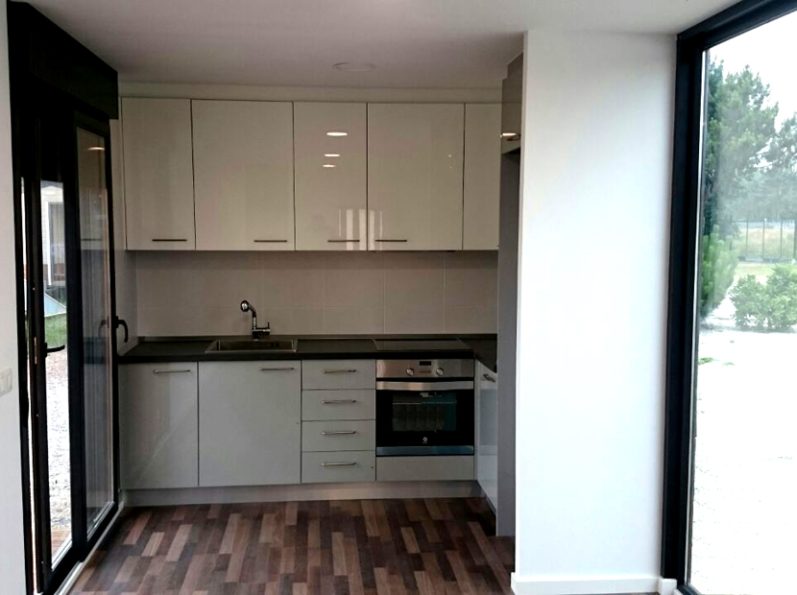 Cocina moderna con muebles blancos, encimera oscura y ventana grande.