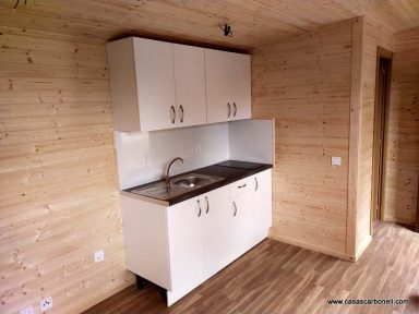 Cocina minimalista con muebles blancos y fregadero en una pared de madera clara.