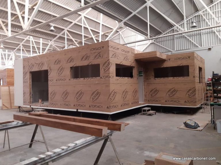 Casa industrializada en construcción con estructura de madera y ventanas en un taller.