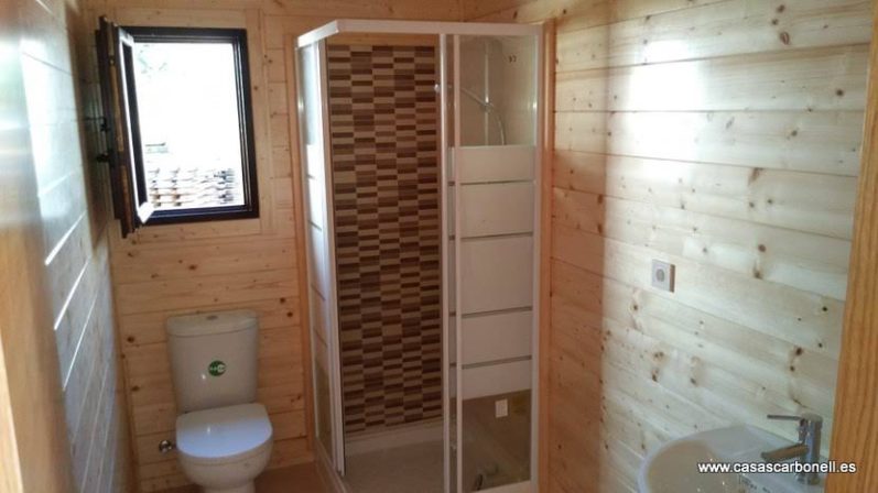 Baño con ducha, inodoro y paredes de madera. Ventana abierta al exterior.
