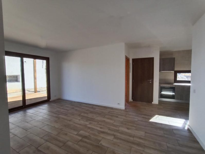 Interior de un salón amplio y luminoso con suelo de madera y acceso a una terraza.