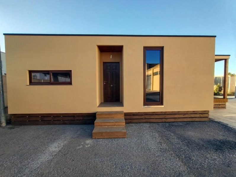 Casa modular de un solo nivel con puerta de madera y ventanas amplias.