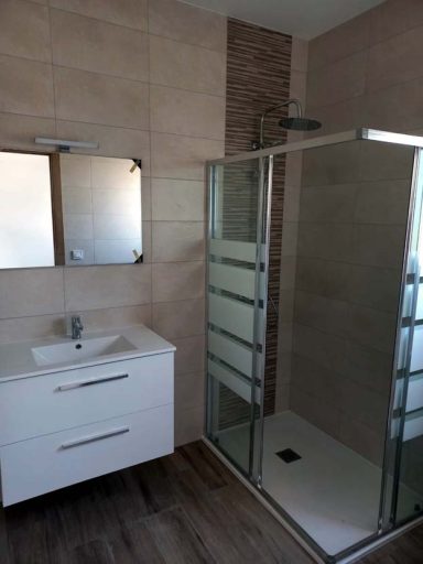 Baño moderno con ducha de cristal y lavabo blanco. Paredes en tonos neutros.