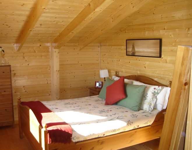 Habitación acogedora con cama doble, paredes de madera y decoración sencilla.