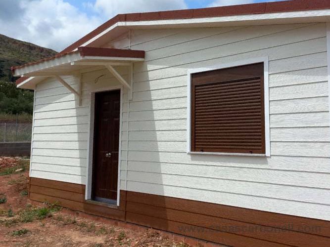 Casa prefabricada con marquesina con exteriores blancos y marrones, ventanas con persianas.