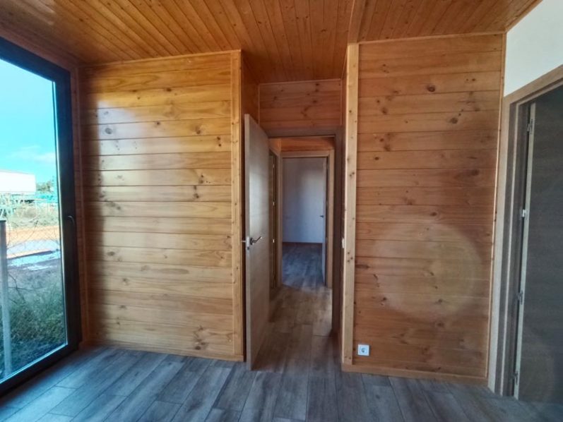 Interior de una habitación con paredes de madera y una puerta abierta al fondo.