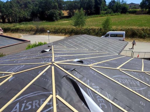 Tejado en construcción, con estructuras de madera y paisaje verde de fondo.