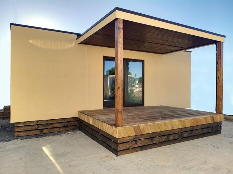 Casa modular de una planta con porche de madera y paredes beige.