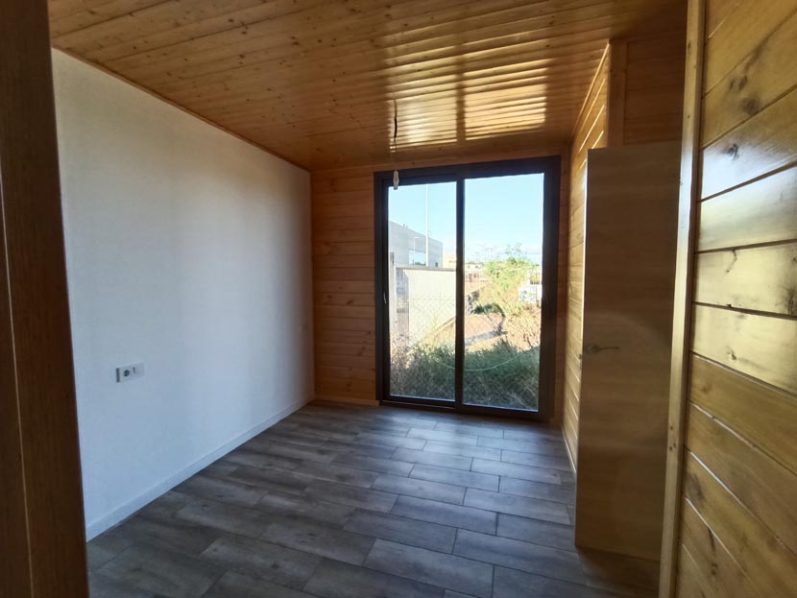 Interior de una habitación con paredes de madera y una ventana grande que asoma a un paisaje.