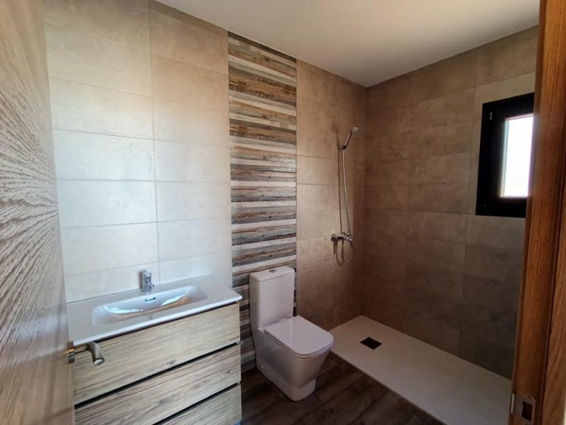 Baño moderno con ducha, inodoro y lavabo, paredes en tonos neutros.