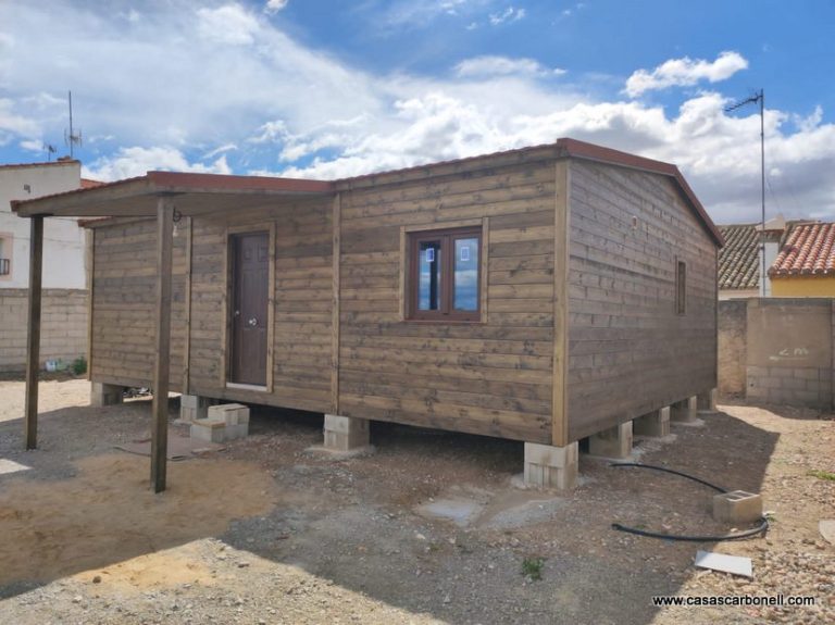 Casa de madera con techo a dos aguas, situada sobre pilotes en un terreno despejado.